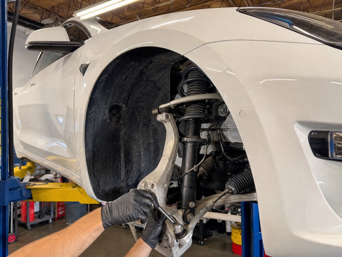 Technician servicing the front suspension on a white Tesla Model 3