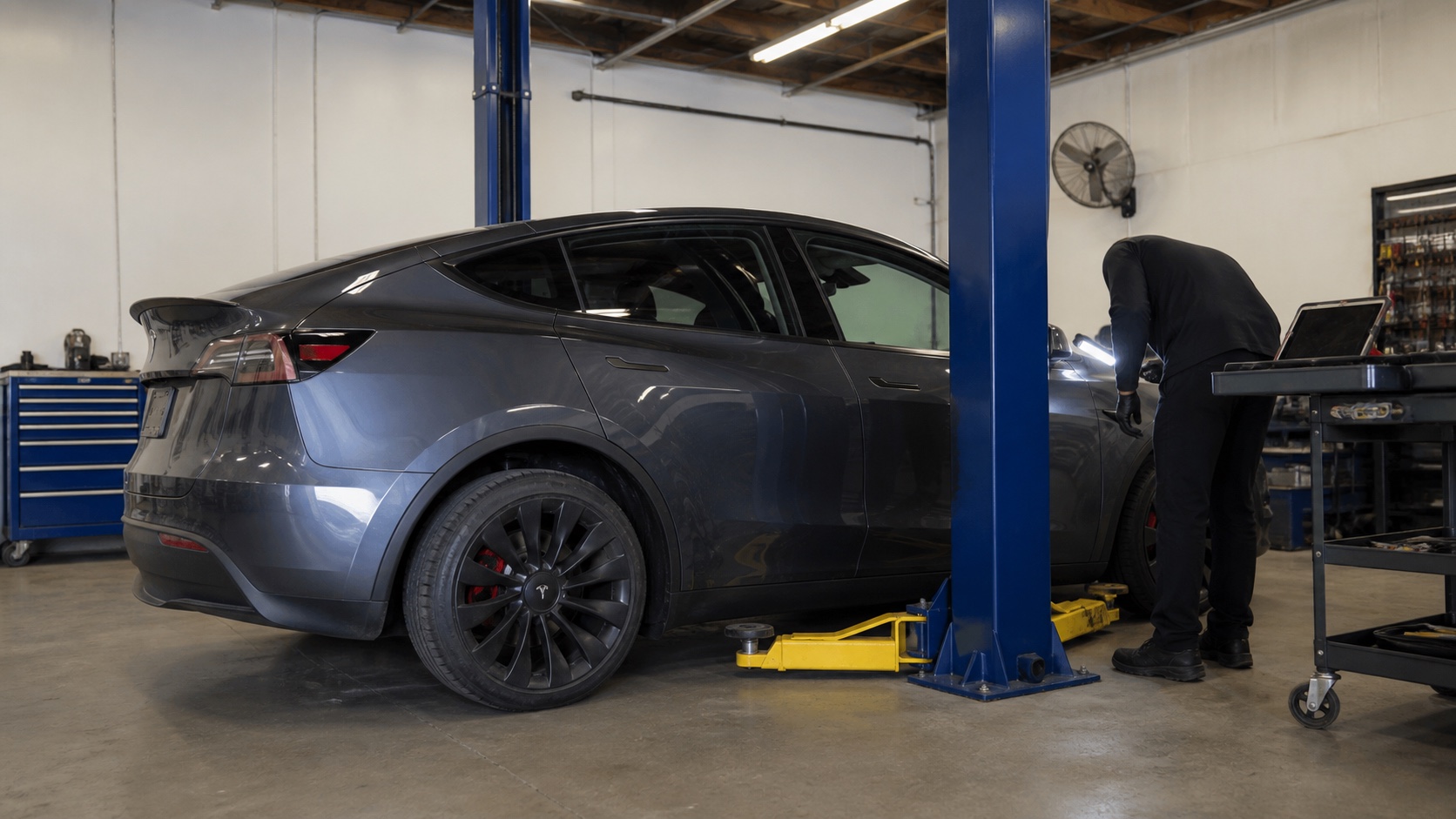 Dark gray Tesla Model Y receiving a mechanical inspection in a service bay